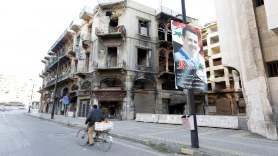 A man rides a bicycle past a poster depicting Syria's President Bashar al-Assad near the new clock square in the old city of Homs, Syria December 7, 2015. REUTERS/Omar Sanadiki -